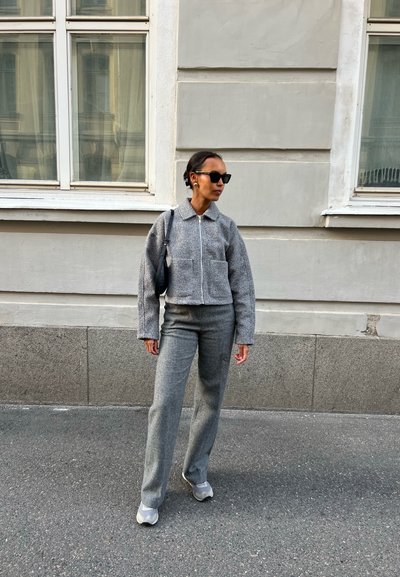 Chaqueta corta gris texturizada con bolsillos frontales y cierre con cremallera, combinada con pantalones rectos grises a juego y zapatillas ligeras.