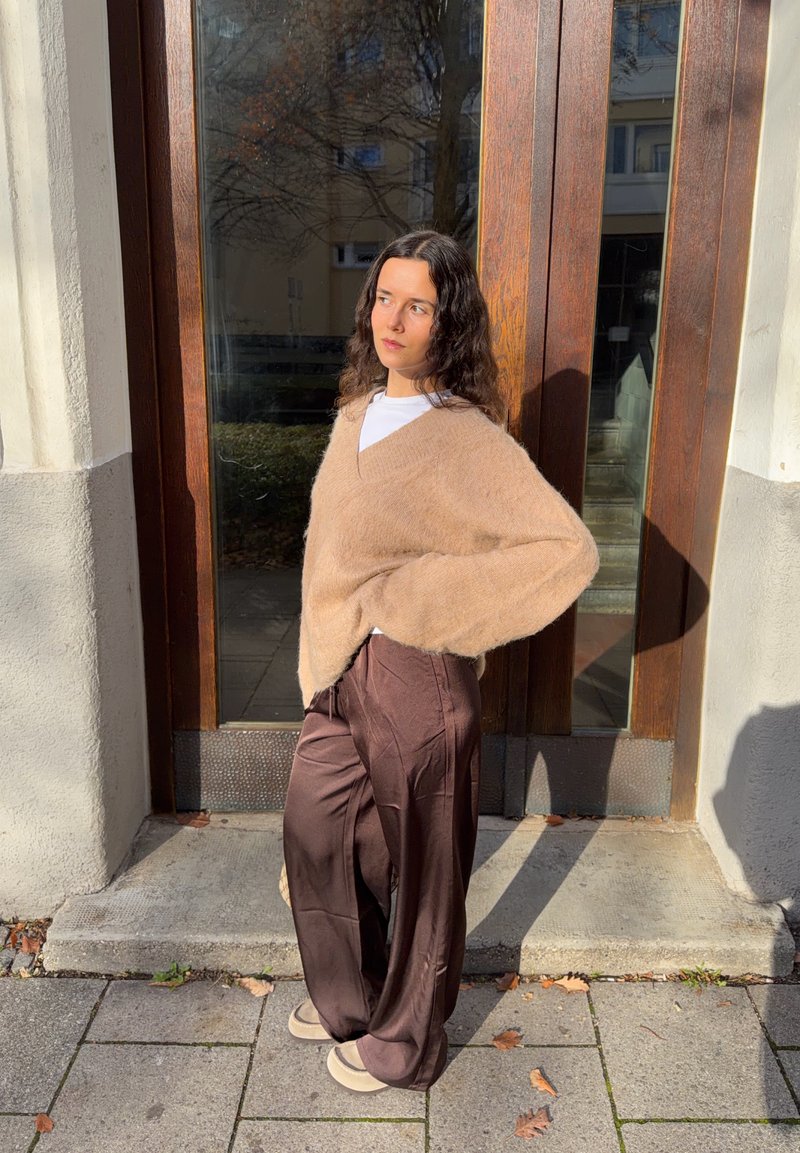 Camisola bege oversize com decote em V e textura suave, combinada com calças largas de cetim castanhas. O conjunto apresenta um ajuste descontraído.