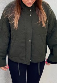 Zelena prešita jakna z visokim ovratnikom, pritrdilnimi gumbi na klik, bočnimi žepi in vrvico na spodnjem robu. Narejena iz teksturirane tkanine. Prijeten, sproščen kroj.