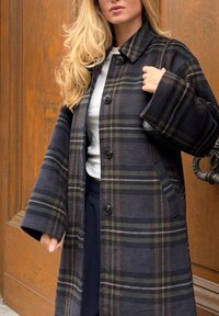 Marineblauer karierten Wollmantel mit großen schwarzen Knöpfen, weiten Ärmeln und Seitentaschen. Das Muster enthält grüne und braune Akzente.