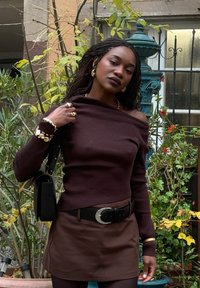 Brun ribbet off-shoulder top kombineret med en brun mininederdel. Accessoirer inkluderer guldbøjler og et sort bælte. Sorte håndtaske fremhæver looket.