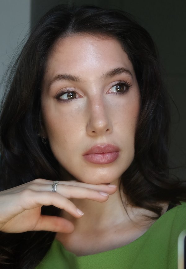 Donna con capelli castani e top verde che poggia il mento sulla mano, indossa un anello d'argento e guarda pensierosa di lato.