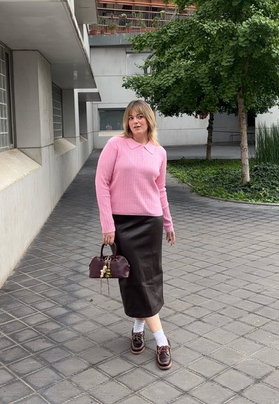 Suéter de canalé rosa con cuello, falda midi de cuero negra, zapatos marrones con cordones, calcetines blancos y un bolso burdeos con adornos.