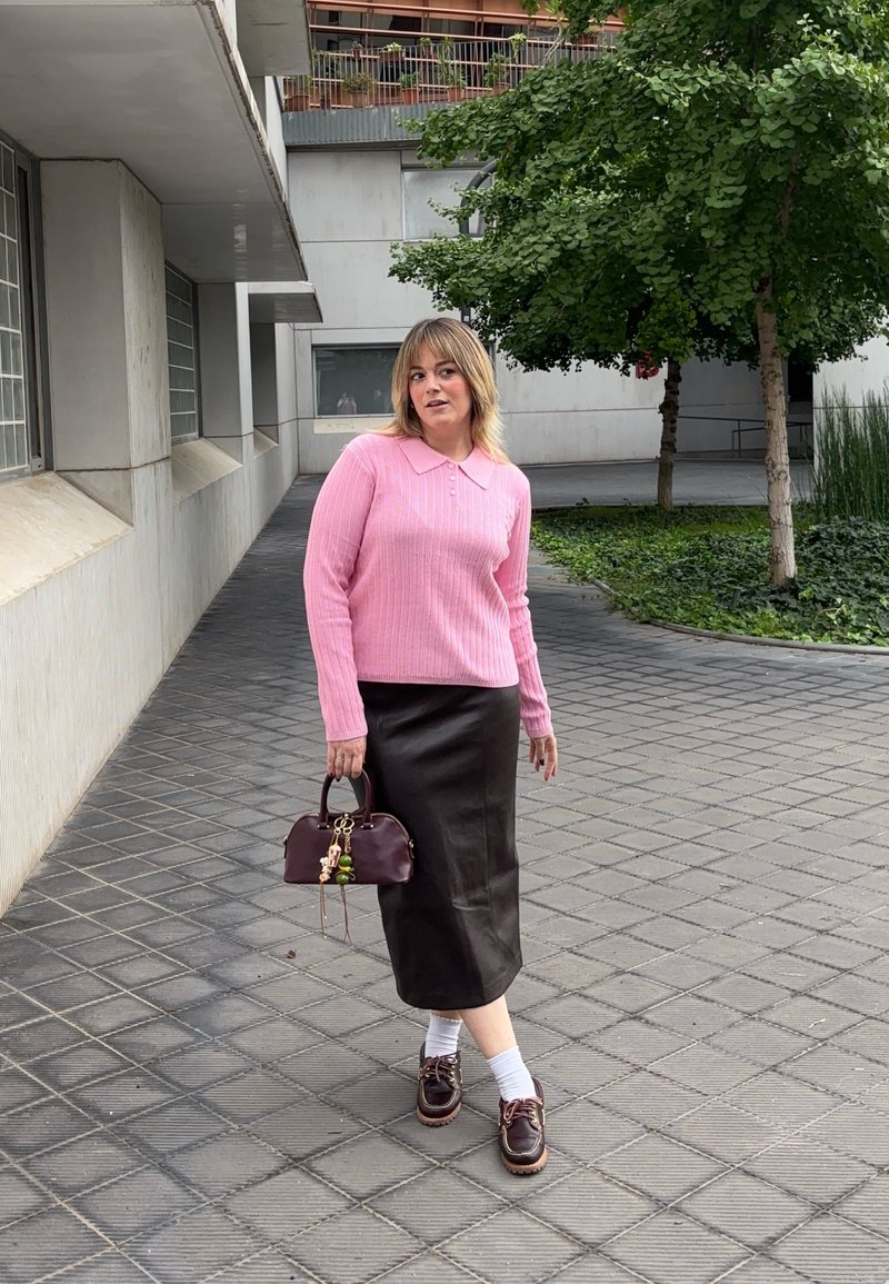 Pink ribbed jumper with a collar, black leather midi skirt, brown lace-up shoes, white socks, and a burgundy handbag with embellishments.