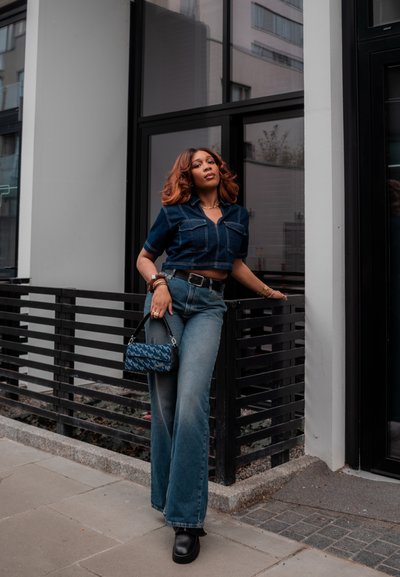 Camisa de denim corta y jeans acampanados de alta cintura, ambos en azul. Accesorios con un bolso de diseño estampado y botas de plataforma negras gruesas.