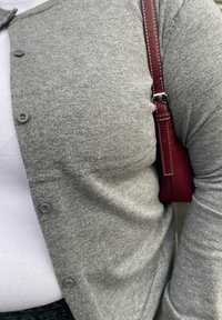 Cardigan tricotat gri cu un front cu nasturi, purtat peste un top alb, asociat cu o geantă burgundă cu bandulieră și detalii de cusătură.