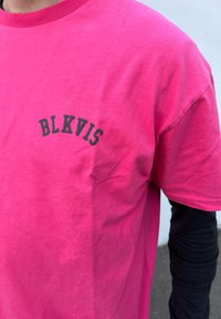 Žiarivo ružové bavlnené tričko s krátkymi rukávmi, s čiernym nápisom "BLKVIS" v oblúkovom dizajne na ľavej časti hrudníka.