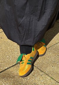 Gule og grønne atletiske sneakers lavet af mesh og suede-materialer, med tre blå striber, en tekstureret sål og grøn snørreklaff.