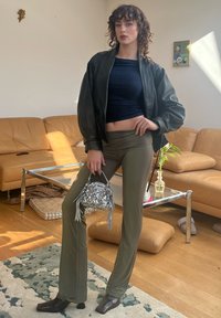 Veste bomber en simili cuir noir sur un haut ajusté bleu marine et un pantalon évasé vert olive. Sac à main en sequins argentés avec des détails à franges.
