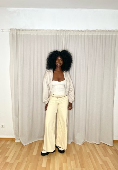 Sudadera de gran tamaño en color crema, blusa blanca de canalé, pantalones anchos crema con cinturón de cadena y zapatos de plataforma negros. Fondo neutro.