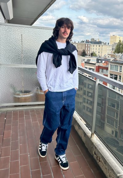 Conjunto informal que incluye una camiseta de manga larga blanca, un suéter azul marino atado al cuello y unos jeans azules holgados con un lavado claro. Zapatillas negras y blancas.