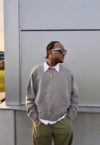 Grå oversized genser med hvit krage, lagvis over en hvit skjorte. Grønne bukser, solbriller og lagdelte halskjeder fullfører antrekket.