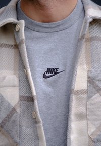 Bežna karirana flanelastih srajca preko sivega majice s krošnjami z črnim vezenim logotipom Nike. Podrobnosti gumbov na srajci.