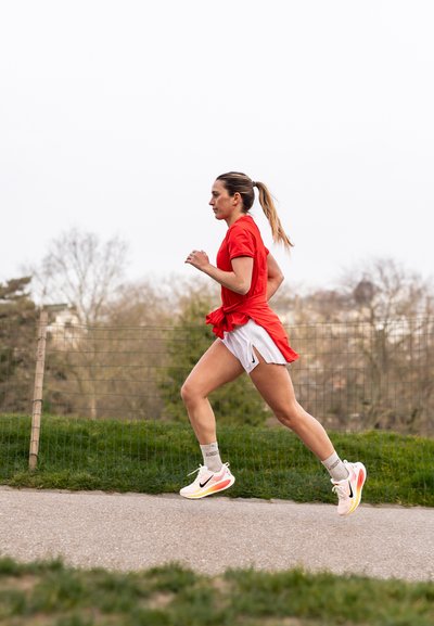 Camiseta de running roja de manga corta, pantalones cortos blancos con aberturas laterales, calcetines deportivos grises y zapatillas de running rosa/ blancas con detalles negros.
