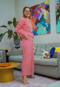 Rdeča in bela črtasta oblačila za sproščanje z dolgimi rokavi in širokimi hlačami. Mehak material, v paru s psom na sivi sedežni in barvitimi umetniškimi deli.