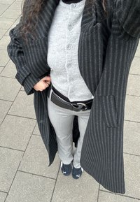 Cappotto a righe nere e grigie sopra un cardigan grigio con bottoni, pantaloni grigi e sneakers nere. Include una cintura nera larga con fibbia argentata.