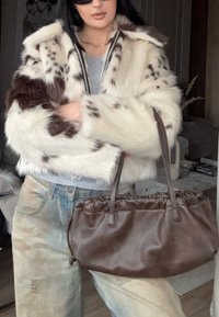 Jakna iz umetnega krzna s kremno-rjavim pikčastim vzorcem, z zadrgo; kombinirana s rjavo torbico z naborki in svetlimi raztrganimi kavbojkami iz jeansa.