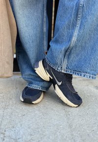 Μαύρα και ναυτικά αθλητικά παπούτσια με υφάσματα από δίχτυ και σουέτ, με κρεμ χρώματος σόλα και ανακλαστικό ασημένιο λογότυπο. Φορεμένα με ανοιχτό μπλε τζιν.