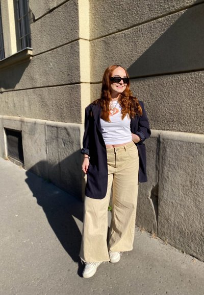 Blazer de rayas marino de gran tamaño sobre una camiseta blanca, combinado con pantalones anchos beige y zapatillas blancas. Los accesorios incluyen gafas de sol negras.