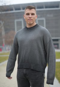 Pull gris côtelé à manches longues, col rond, avec un design raccourci et texturé, associé à un jean gris foncé.