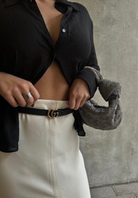 Camisa preta de botões, saia lápis branca, cinto preto com fivela GG dourada e bolsa tecida cinza. Enfoque nas texturas dos tecidos e nas cores.