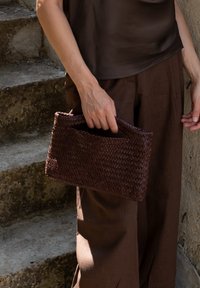 Wielokolorowa brązowa torebka o prostokątnym kształcie, z teksturowaną powierzchnią i otwartym wierzchem. Trzymana przez osobę w brązowych spodniach i bluzce.