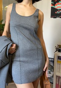 Szara sukienka bez rękawów wykonana z miękkiego materiału, o dopasowanym kroju, z detalami przeszyć i dekoltem w serek, zestawiona z szarą kurtką.