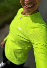 Top sportivo verde lime caratterizzato da un motivo testurizzato e piccole perforazioni, con un logo bianco sul petto. Maniche lunghe e design aderente.