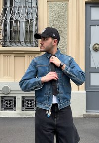 Džínová bunda se světlemodrým a tmavěmodrým pruhovaným vzorem, s límečkem a zapínáním na knoflíky. Nositá přes bílou košili a černé kalhoty.