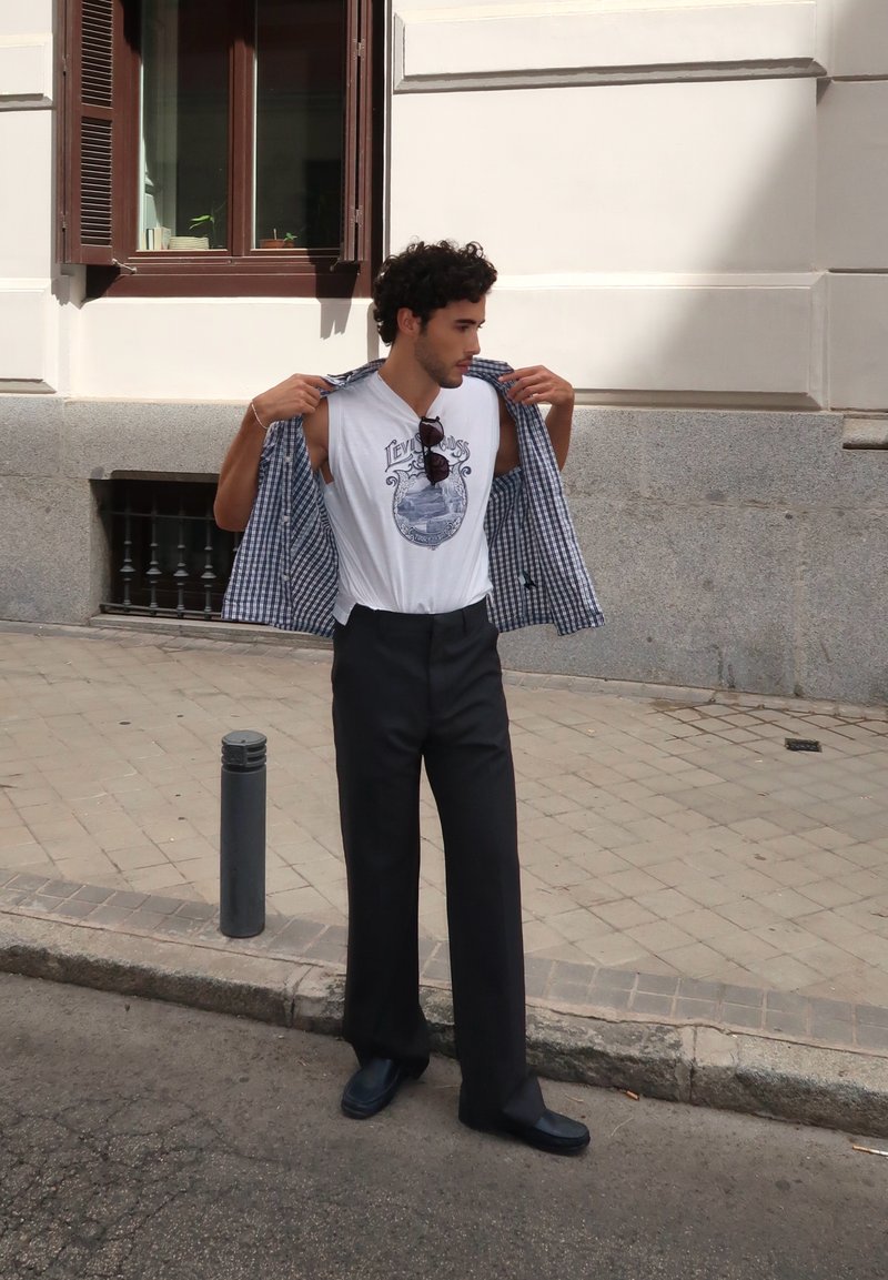 T-shirt branco com uma impressão gráfica, combinado com calças largas azul-marinho e uma camisa xadrez. Mocassins pretos completam o visual.