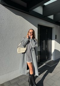 Palton gri din lână, rochie cu dungi, cizme negre până la genunchi și o geantă crem de tip crossbody. Textură moale și design modern pe un fundal deschis la culoare.