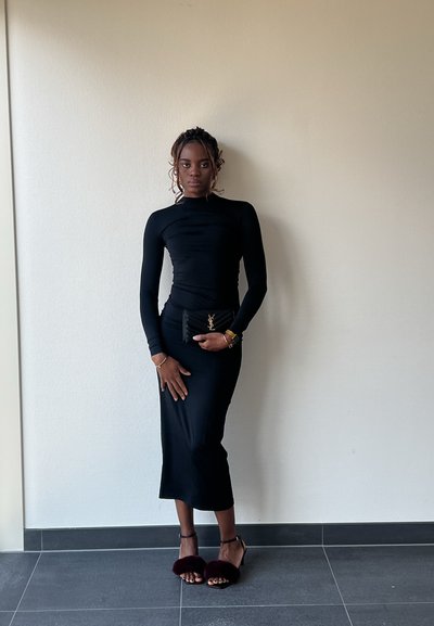 Top negro de manga larga con una silueta ajustada, combinado con una falda negra de longitud media. Acentuado con un bolso negro que presenta un logo dorado y tacones esponjosos en burdeos.