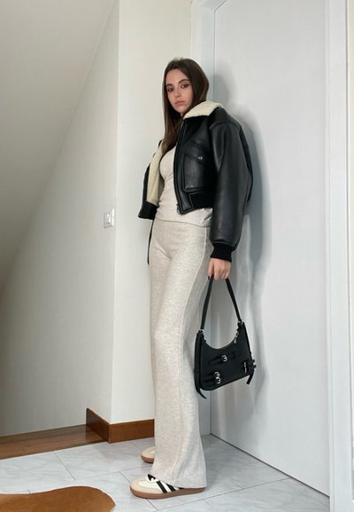 Chaqueta de cuero negra con cuello de shearling, parte superior ajustada gris, pantalones acampanados grises, zapatillas blancas con rayas negras, bolso negro.