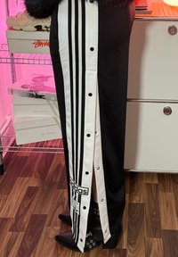 Fekete sportos szoknya fehér oldalsávokkal, patentos részletekkel és Adidas logóval. Fekete bokacsizmával viselve, mely díszes fémkiegészítőkkel rendelkezik.