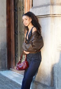 Übergroße braune Lederjacke mit geripptem Bund, schwarzes Paillettenoberteil, hoch taillierte dunkle Jeans und eine rote Schultertasche.