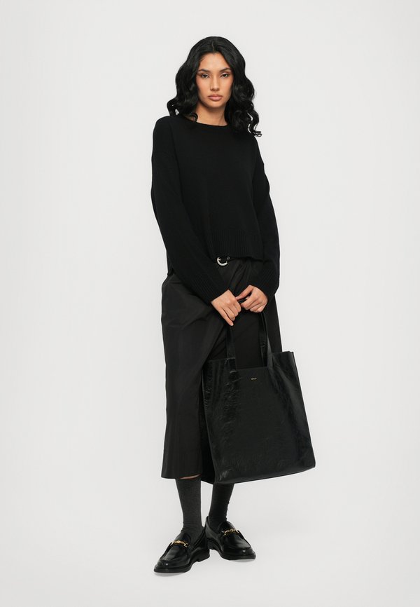 Maglione nero lavorato a maglia con maniche lunghe, abbinato a pantaloni neri larghi e una borsa a tracolla nera lucida. Il modello indossa mocassini neri e calzini grigi.