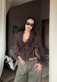 Cardigan maro pufoasă, scurtă, cu decolteu adânc în V, asortată cu pantaloni largi verde măsliniu; ține o geantă mică maro. Ochelarii de soare completează ținuta.