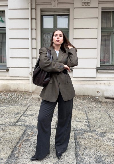 Blazer de cuadro marrón de corte oversize sobre una blusa blanca, combinado con pantalones de pierna ancha gris oscuro y zapatos negros de punta. Bolso de cuero marrón.