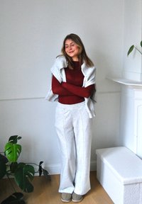 Helle graue Jogginghose mit Seitennähten, kombiniert mit einem bordeauxfarbigen Langarmoberteil. Ein heller grauer Pullover ist über die Schultern gelegt.