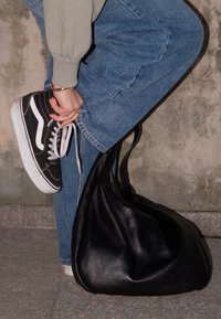 Črne platnene superge z belimi detajli, modri jeans in velika črna usnjena torba. Torba je sproščena z lesketajočo teksturo in zadrgo.