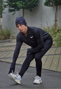 A fekete sportos öltözet hosszú ujjú felsőből, nadrágból és Nike logós kesztyűkből áll. Egy sapka egészíti ki az öltözetet. Teljesítménycipők kiemelve.