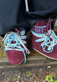 Burgunderrøde semskede ankelstøvler med rund tå, med blå og kremfargede lisser og "NOON BOOT"-merke på et lyseblått bånd.