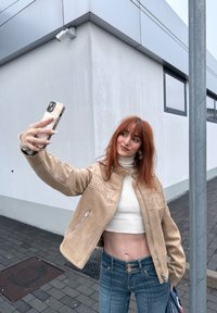 Beige faux leather jacket featuring embroidered text reading "EASY" and "FUEL", high collar, silver zipper, teamed with a white cropped sweater and blue jeans.