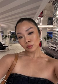 Denim strapless top, leather shoulder strap, pearl necklace, and large earrings. Light skin tone, straight hair, indoors with patterned walls.