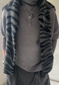 Pull gris à texture côtelée, superposé d'un châle à rayures noires. Colliers en argent avec une clé décorative et un pendentif. Pantalon gris foncé.