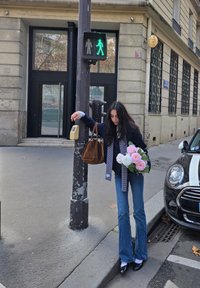 Közlekedési lámpa zöld gyalogos jelzéssel; egy személy rózsaszín és fehér virágcsokrot tart, farmert visel, amely szárában bővül, és sötétkék dzsekit.