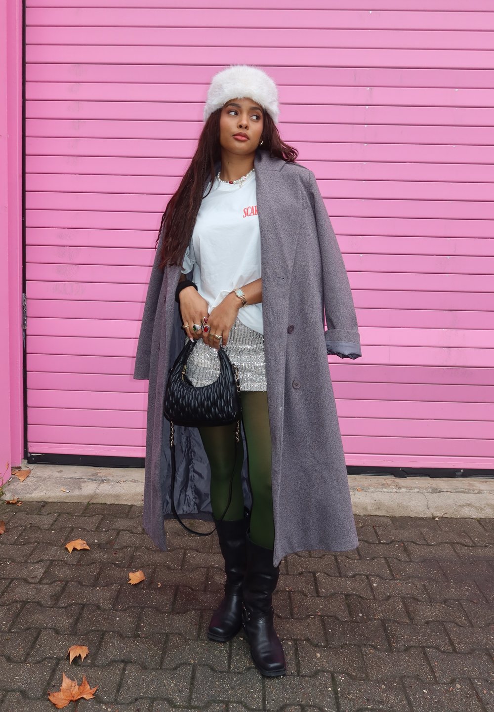 Γκρι παλτό, λευκό μπλουζάκι με κόκκινο κείμενο, λαμπερή ασημένια μίνι φούστα, πράσινες καλσόν, μαύρες μπότες έως το γόνατο και μια μαύρη υφασμάτινη τσάντα. Λευκό καπέλο με γούνα.