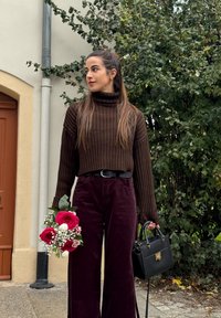 Brown ribbed turtleneck jumper, wide burgundy corduroy trousers, black handbag, and a bouquet of red roses with greenery.