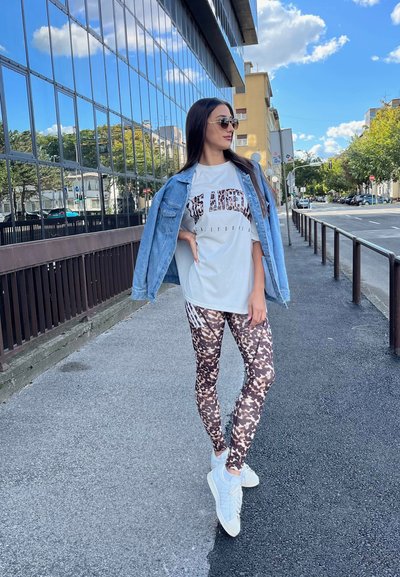 Camiseta gráfica blanca con el texto "Los Ángeles", combinada con leggings de camuflaje marrón y una chaqueta de denim azul claro, complementada con zapatillas blancas.