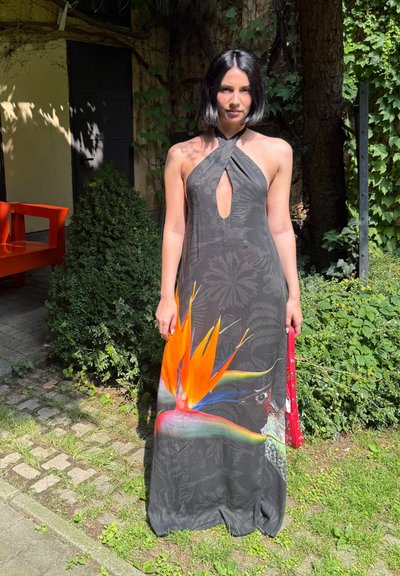 Largo vestido negro sin mangas con un patrón de hojas y un gráfico vibrante de ave del paraíso en naranja y verde en la parte inferior.
